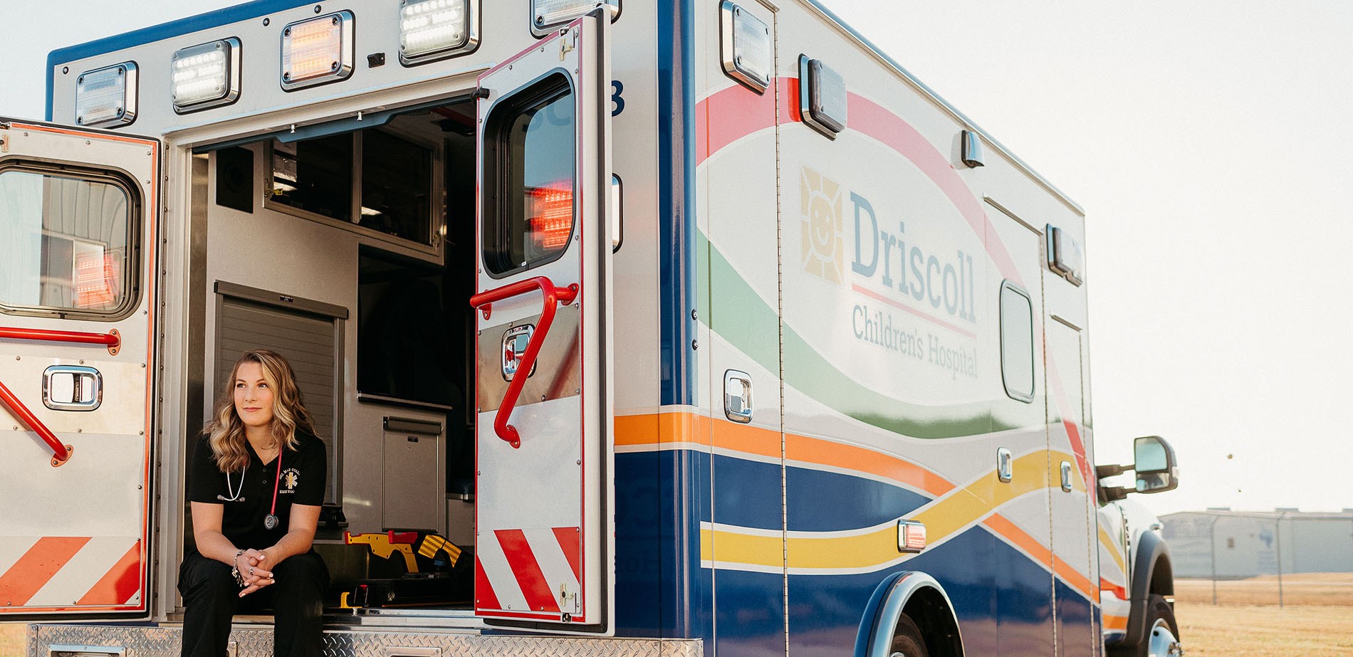 DMC Graduate Mackenzie Scott sitting in the open rear door of an ambulance