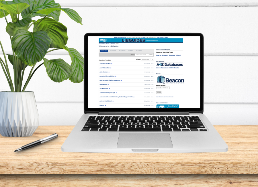 A laptop computer on a desk with a pen and a plant sitting on the desk